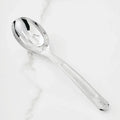 The 10.5-inch Stainless Steel Slotted Serving Spoon from Hestan Provisions® rests on a white marble countertop, its reflective surface gleaming.