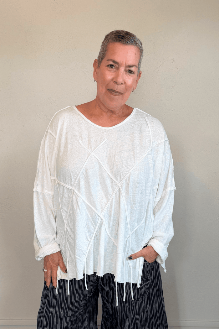 Oversized long-sleeve corded top shown in black and white, with a wide round neckline, dropped shoulders, abstract raised cord detailing across the front, an uneven raw-edge hem, and hanging cord accents.