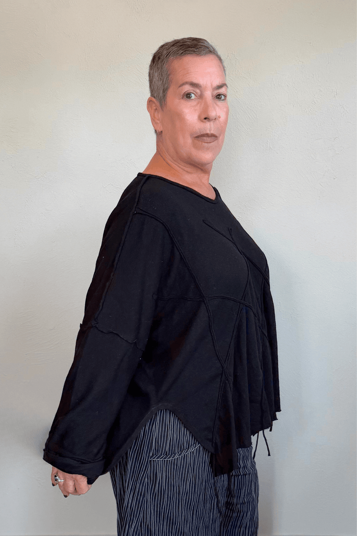 Oversized long-sleeve corded top shown in black and white, with a wide round neckline, dropped shoulders, abstract raised cord detailing across the front, an uneven raw-edge hem, and hanging cord accents.