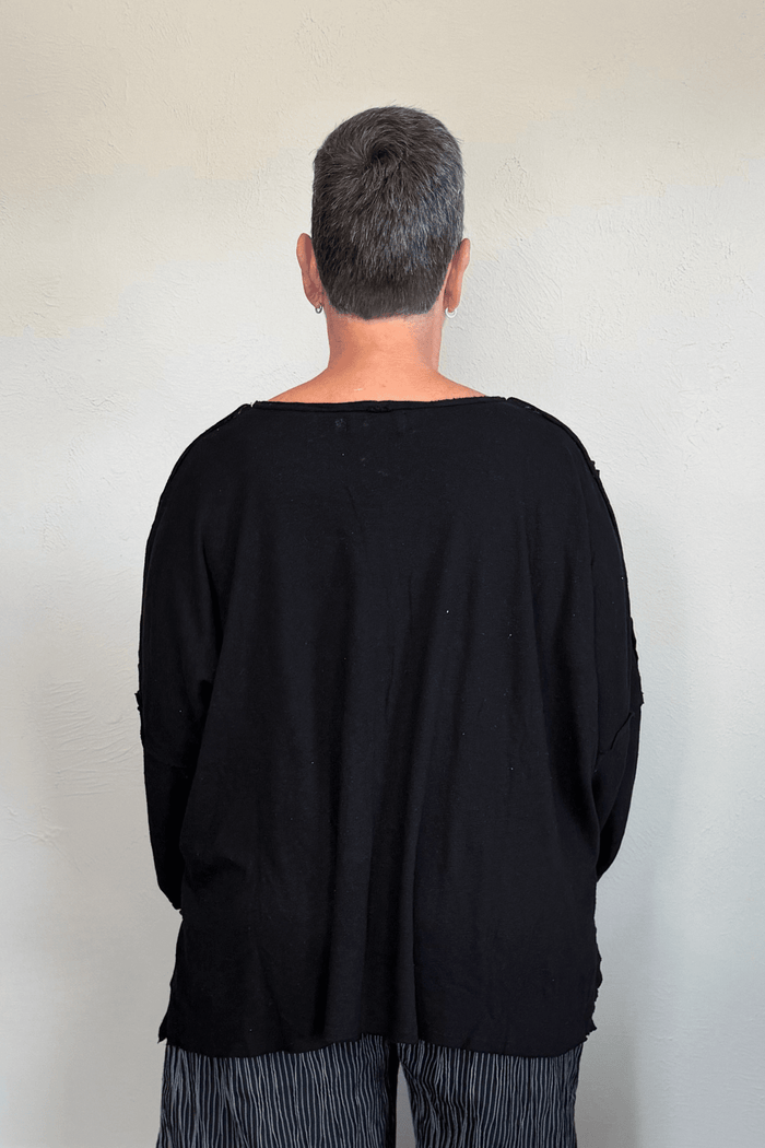 Oversized long-sleeve corded top shown in black and white, with a wide round neckline, dropped shoulders, abstract raised cord detailing across the front, an uneven raw-edge hem, and hanging cord accents.