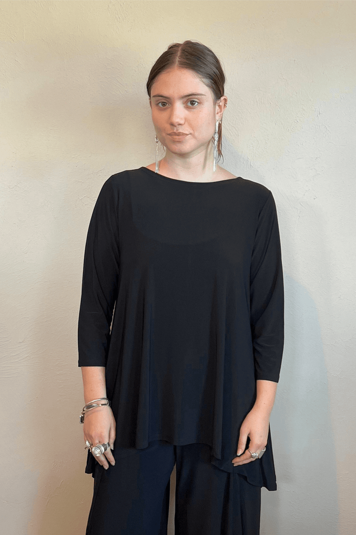 Model wearing the black Kozan Dima tunic with a boat neckline, three-quarter sleeves, and an asymmetrical draped hem, shown from front and back.