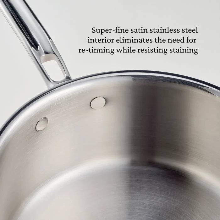 Close-up of the CopperBond Aura™ Polished Copper 0.75-Quart Butter Warmer, showcasing its gleaming stainless steel interior with a super-fine satin finish and two sturdy rivets on the side. Text beside the pan highlights its stain-resistant surface, which eliminates the need for re-tinning—features typically reserved for professional-grade copper cookware.
