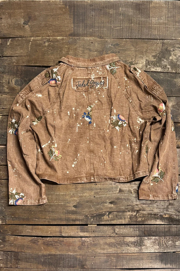 Brown cropped cotton jacket with floral embroidery, paint-splatter detailing, notched lapel collar, button front, and long sleeves with cuff tabs; back view shows center seam and Jaded Gypsy patch.