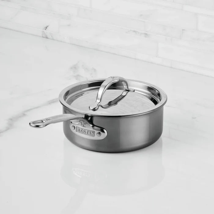 A NanoBond® Titanium Saucepan with a lid rests on a white marble countertop in a modern kitchen. This titanium stainless steel saucepan features a sleek metal handle and polished finish, with the NanoBond® brand name clearly visible on the side.