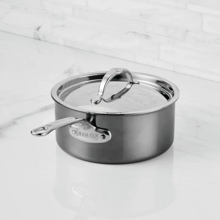 A NanoBond® Titanium Saucepan with a matching lid rests on a white marble countertop. The pan features a long handle and a sturdy, rounded design with a polished finish, highlighting the advanced durability of molecular titanium cookware.
