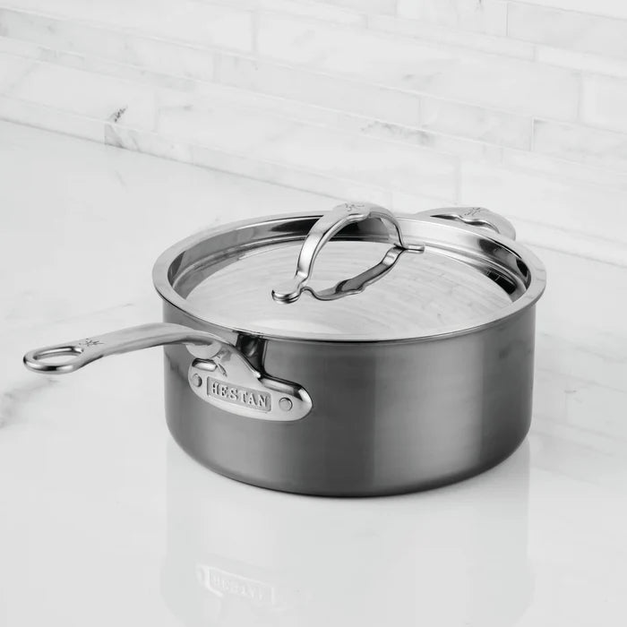 A NanoBond® Titanium Saucepan with a fitted lid rests on a marble countertop. The titanium stainless steel saucepan features a long handle and a smaller loop handle, both secured with visible screws. The NanoBond® brand name is engraved on the handle near the body, showcasing its status as premium titanium cookware.